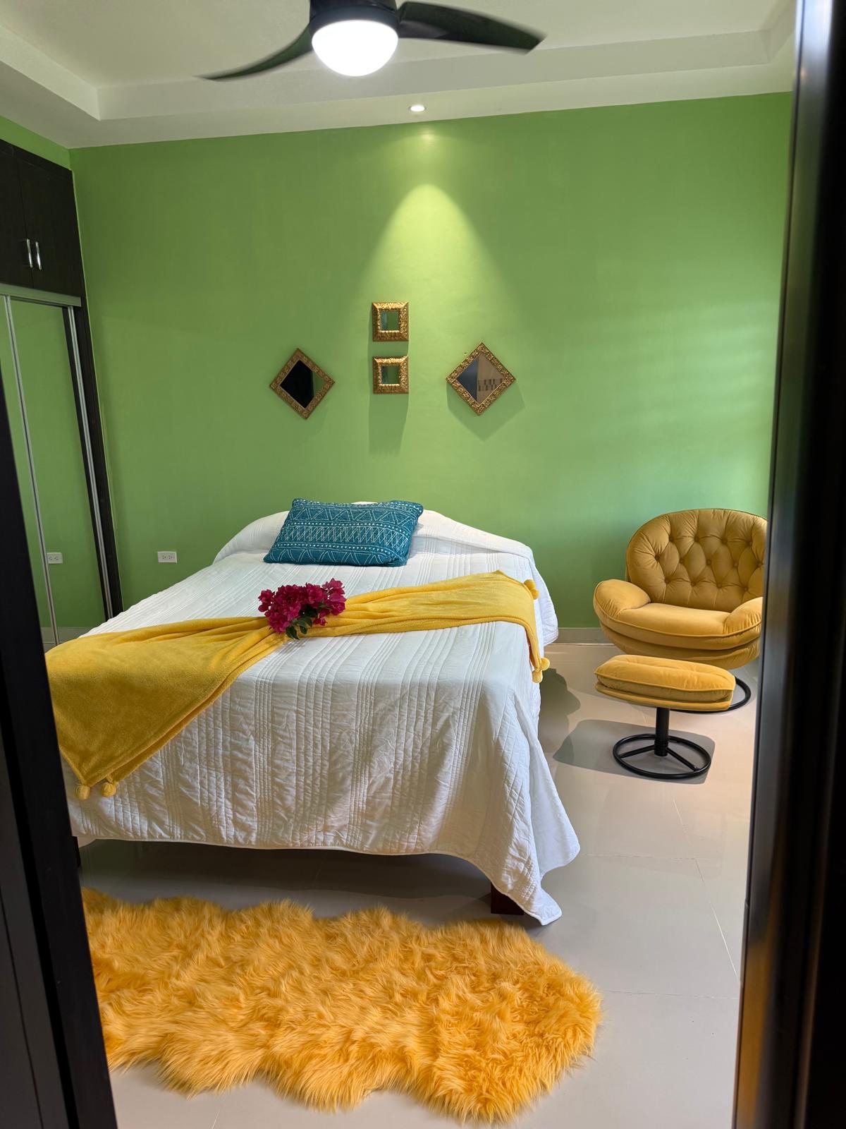 Bedroom with green accent wall and yellow lounge chair